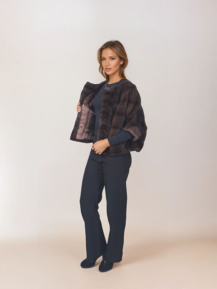 Angled front view of a model wearing Tulle in brown mink with black pants, holding it open to show the lining.