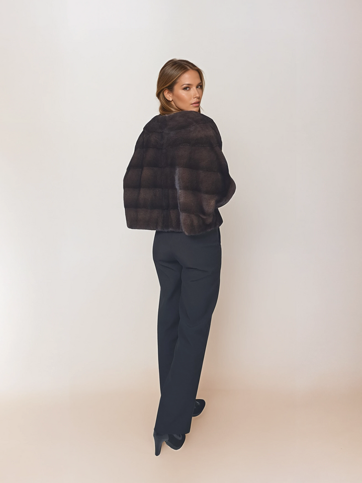 Angled back view of a model wearing Tulle in brown mink with black pants, looking over her shoulder.